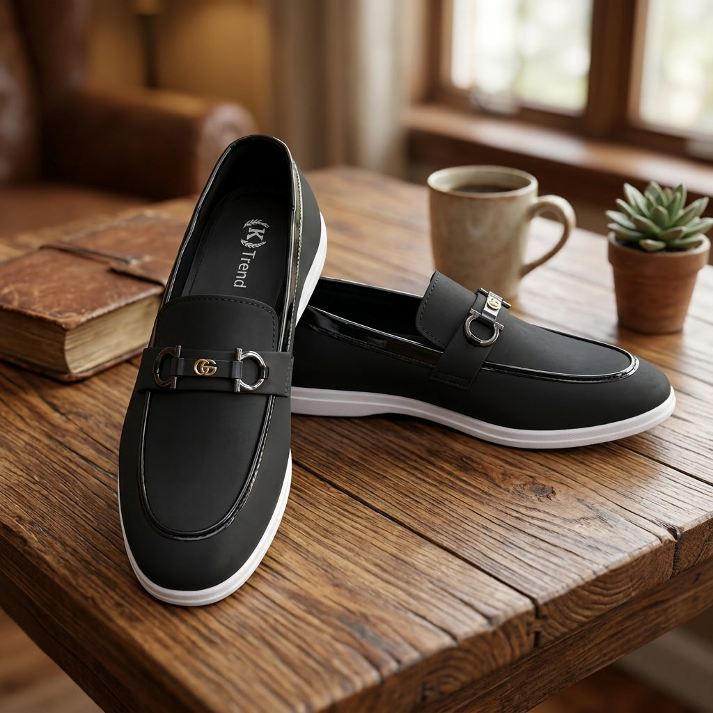 Black leather horsebit sneaker loafer pair on rustic wooden table lifestyle shot with coffee mug book and succulent plant