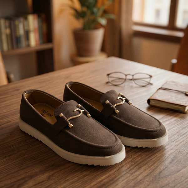 Dark chocolate suede horsebit sneaker loafer pair on walnut wooden desk lifestyle shot with reading glasses and leather journal
