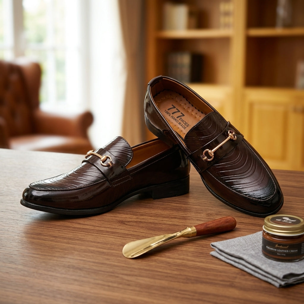 Dark brown patent wave-texture horsebit loafer pair on wooden table lifestyle shot with shoe care accessories
