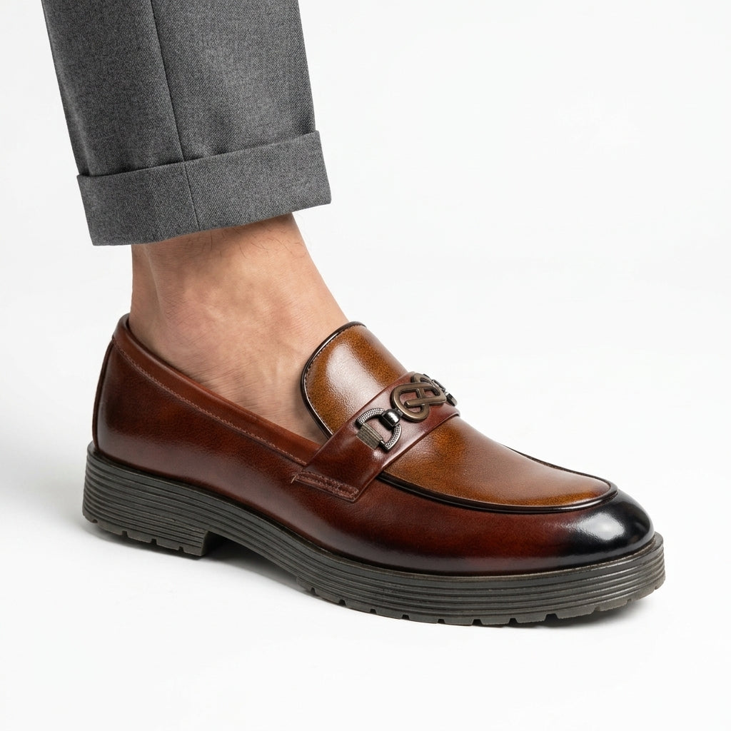 Tan burnished leather chunky-sole loafer with gunmetal logo hardware worn with grey trousers