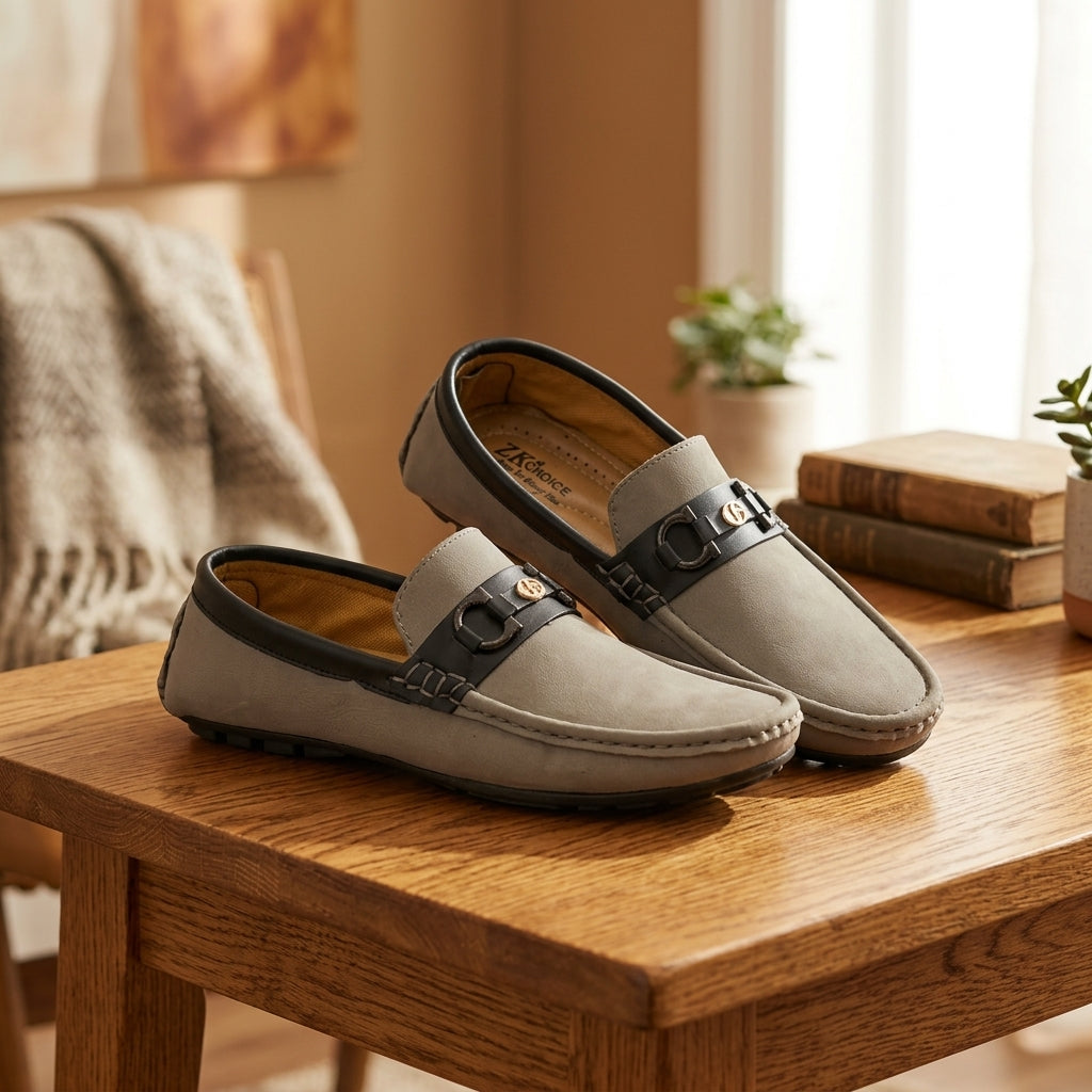 Grey nubuck two-tone horsebit driving loafer pair on wooden table warm lifestyle setting with books and throw blanket