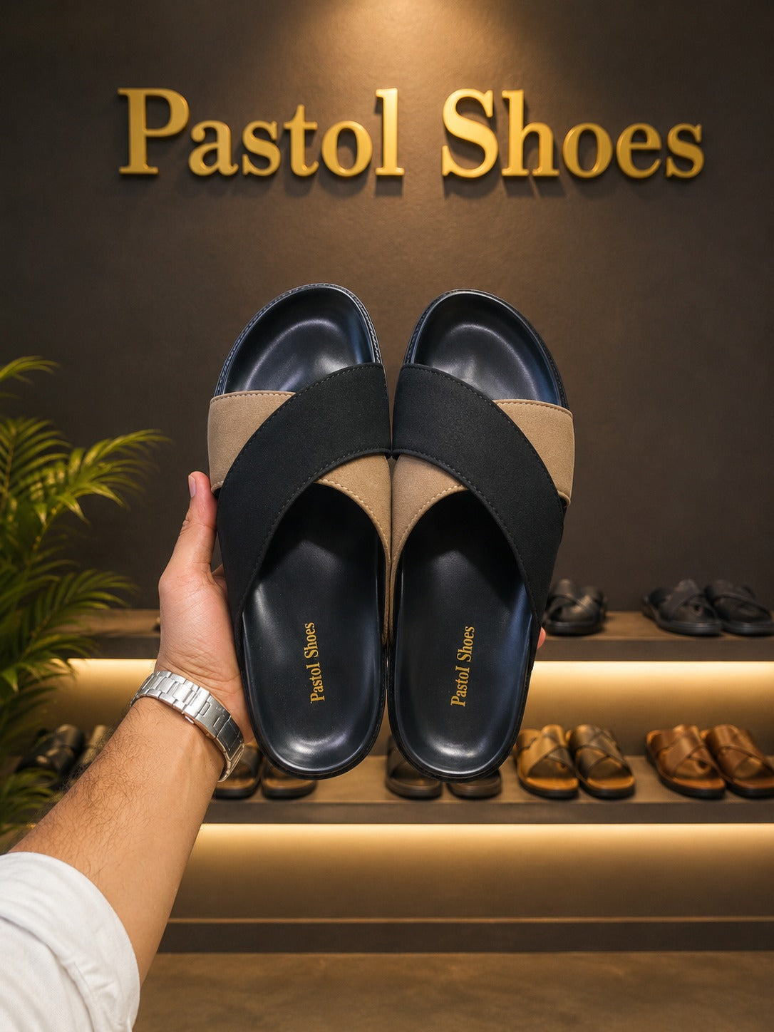 Navy and tan two-tone cross-band leather slide sandal pair standing upright against matte black Pastol Shoes gift boxes on marble floor in luxury shoe boutique warm lit shelving