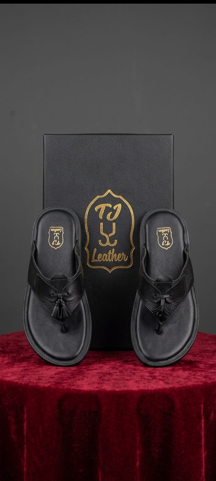 Black leather tassel medallion T-bar flip sandal pair top-down on crimson velvet plinth with matte black TJ Leather gift box luxury presentation shot