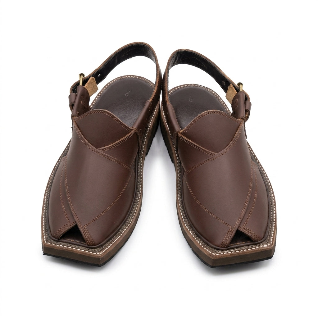 Dark brown cross-strap Kaptaan Peshawari chappal worn on stone courtyard with cream shalwar kameez gold buckle visible