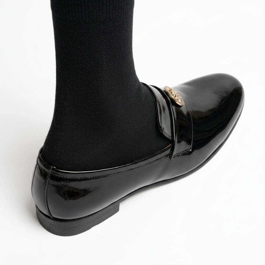 Black patent leather loafer with gold medallion worn by man with black socks