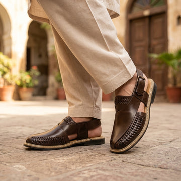 Dark brown leather Peshawari woven slingback sandal worn on cobblestone street with cream shalwar trousers