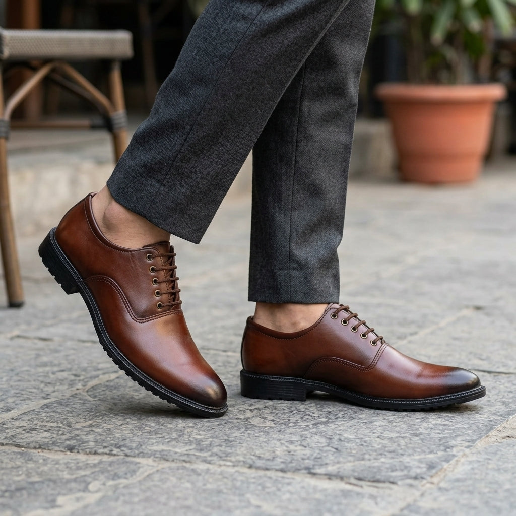 Brown leather plain-toe derby dress shoe worn outdoors on cobblestone with grey trousers