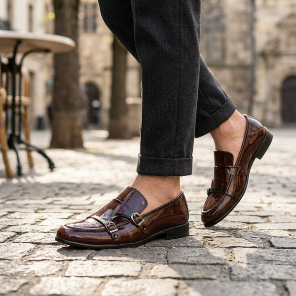 Brown patent leather double monk-strap loafer worn on cobblestone street with rolled dark trousers