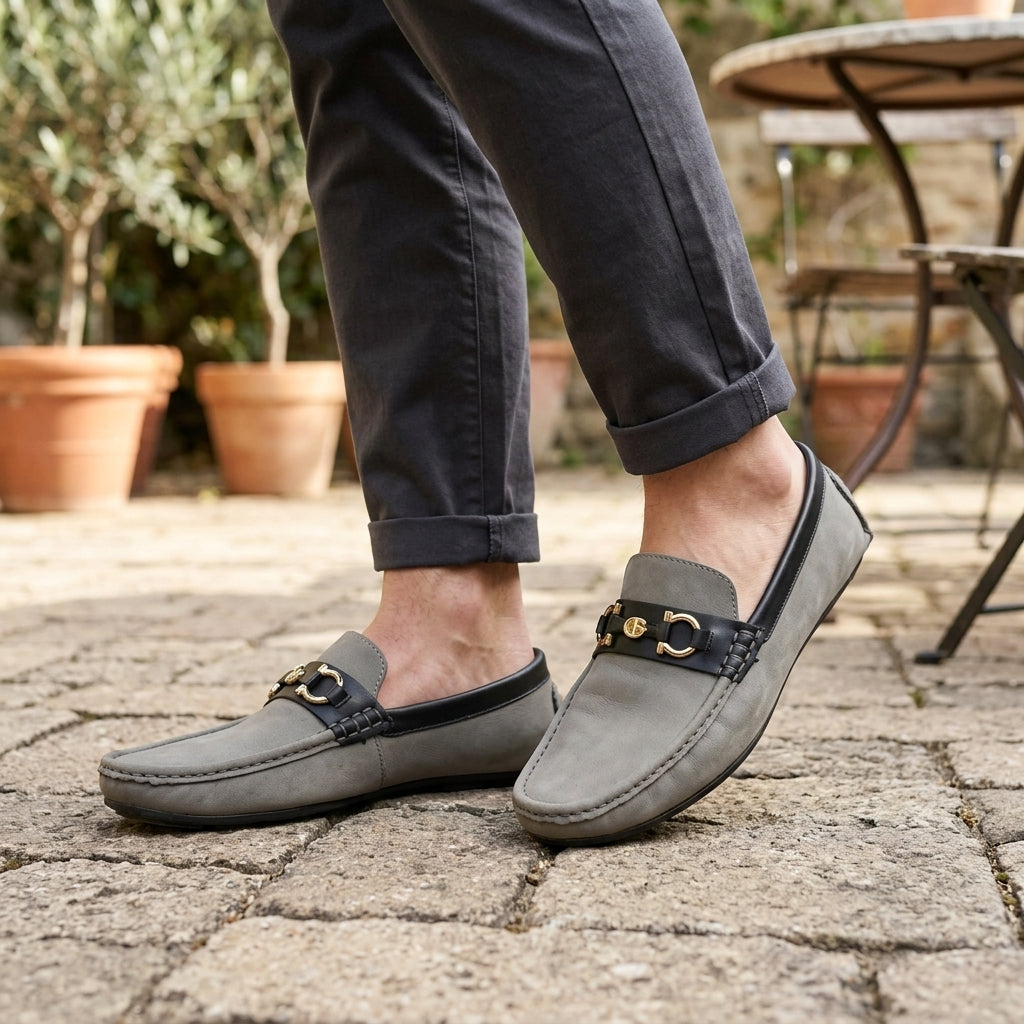 Grey nubuck two-tone horsebit driving loafer worn on cobblestone terrace with rolled charcoal chinos outdoor setting