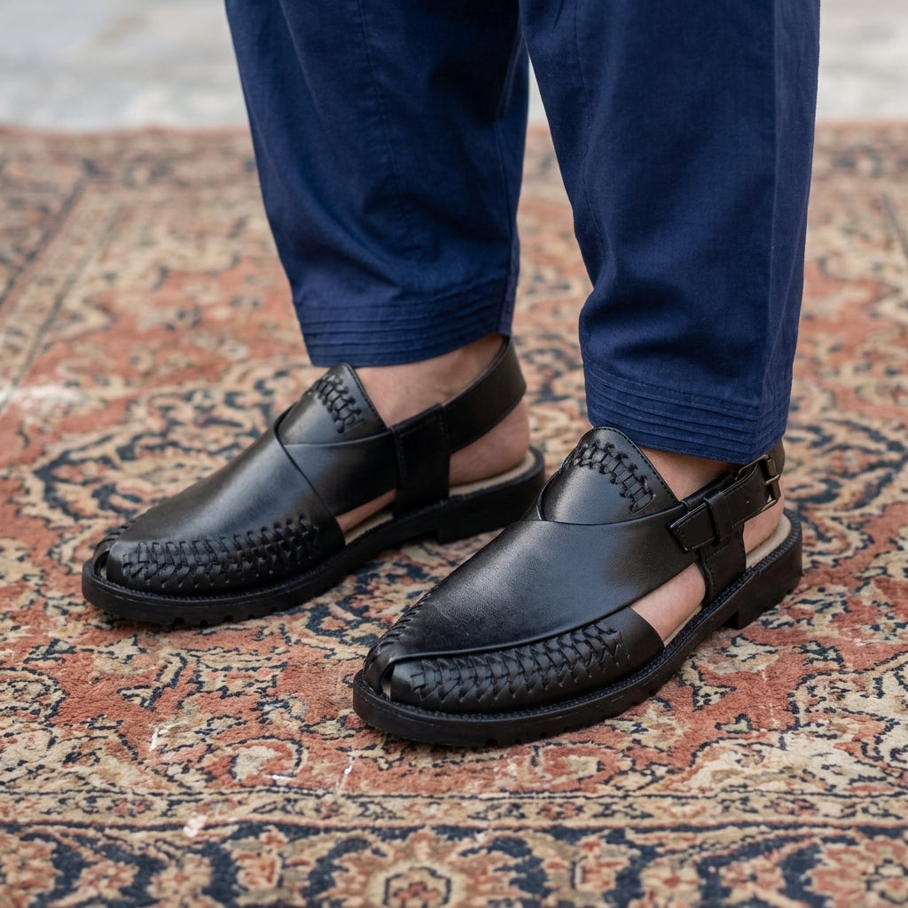 Black leather woven-trim Peshawari slingback chappal worn on traditional carpet with navy shalwar kameez