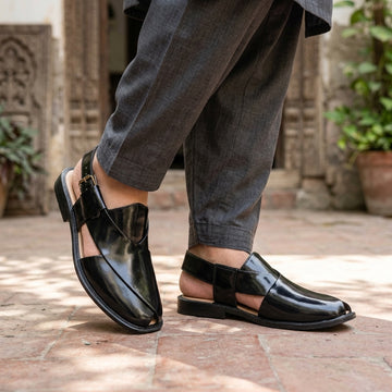 Black patent leather Kaptaan Peshawari chappal worn on terracotta brick haveli courtyard with charcoal grey shalwar kameez mid-stride